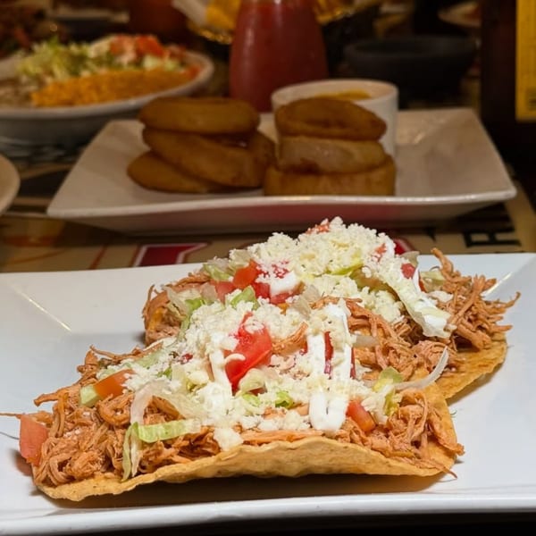 Two tostadas topped with shredded chicken, lettuce, tomatoes, cheese, and sour cream at Casa Jalisco.
