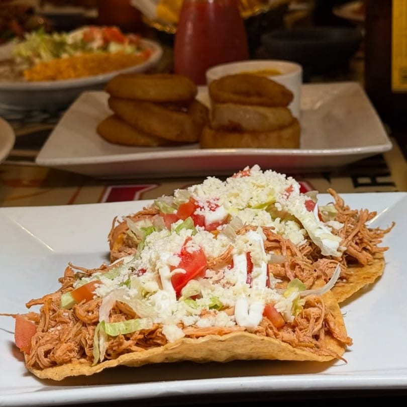 Two tostadas topped with shredded chicken, lettuce, tomatoes, cheese, and sour cream at Casa Jalisco.
