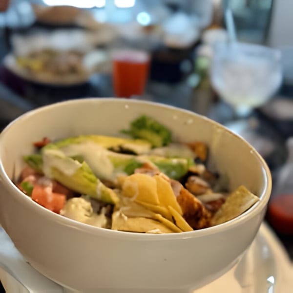 A white bowl of Casa Jalisco's Mexican salad with avocado, tortilla strips, and dressing.