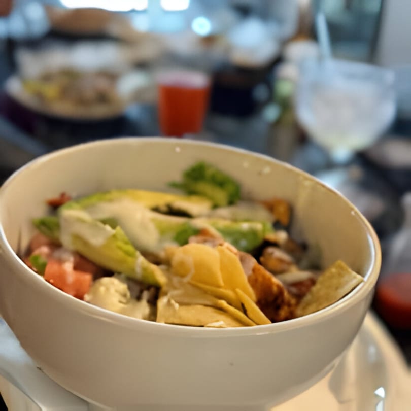 A white bowl of Casa Jalisco's Mexican salad with avocado, tortilla strips, and dressing.