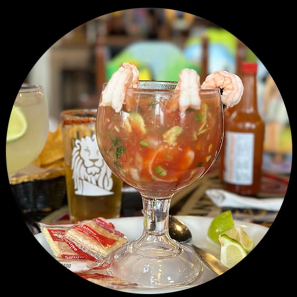 Shrimp cocktail in a goblet with lime, saltine crackers, and hot sauce on a table.