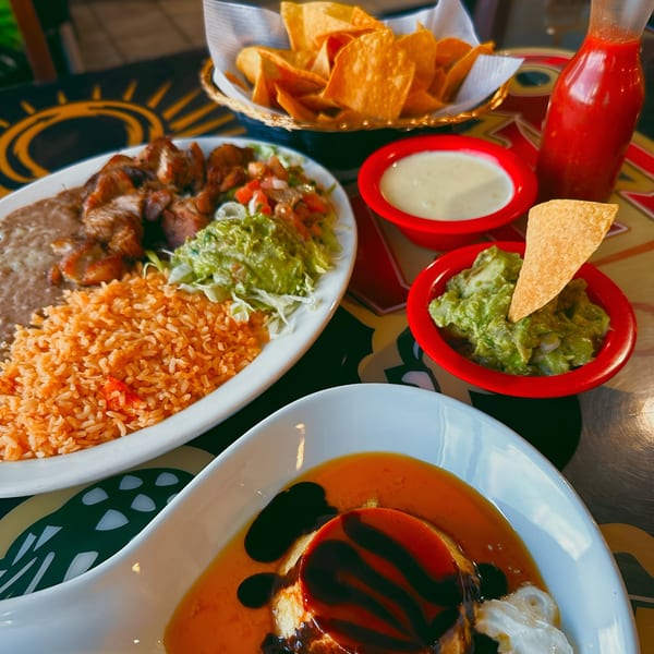 A Mexican meal with chicken, rice, beans, guacamole, chips, salsa, queso, and flan.
