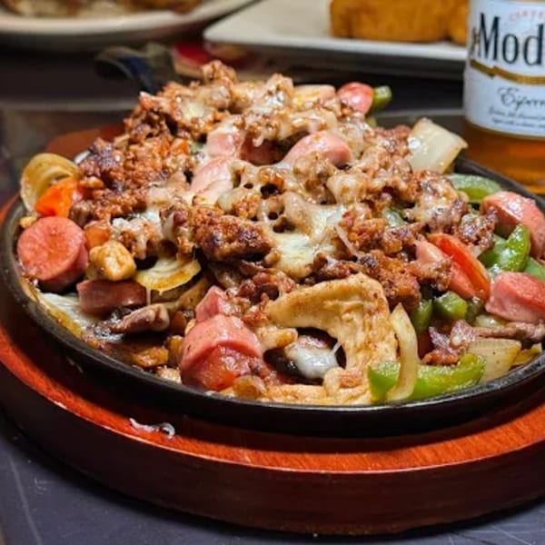 Sizzling Mexican fajitas with chorizo, hot dogs, bell peppers, and onions, topped with melted cheese.