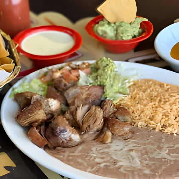 A Mexican carnitas platter with rice, refried beans, guacamole, and a side of queso dip.