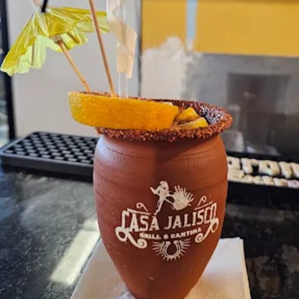 A Casa Jalisco branded clay mug with a drink, garnished with orange slices and a yellow umbrella.